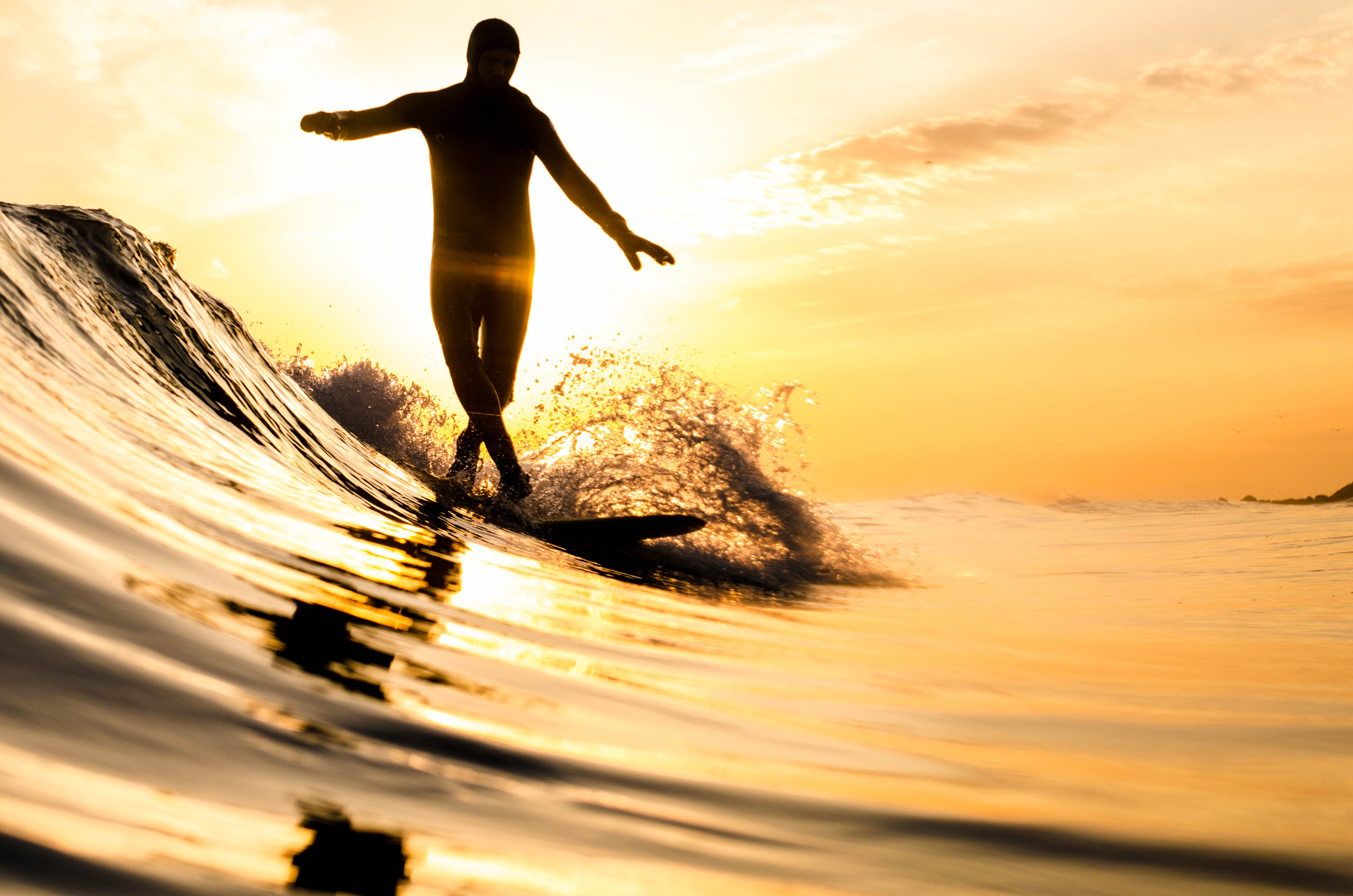 Completely Fun Socially Distanced Activities for Your NYC Winter: A surfer cross-stepping on a longboard in New York during a small winter swell during sunset
